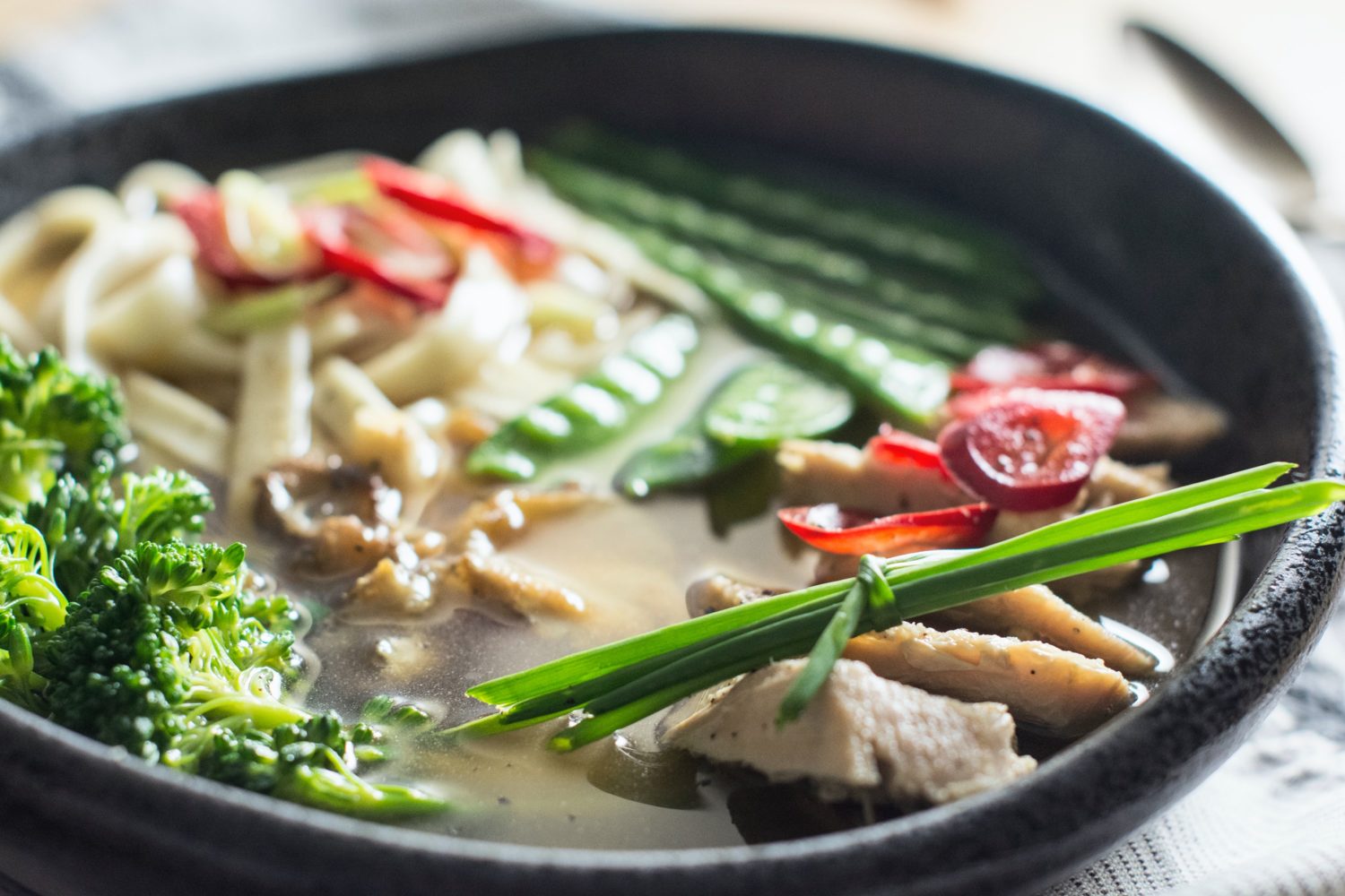 image of soup with noodles, broccoli, snow peas and chilis