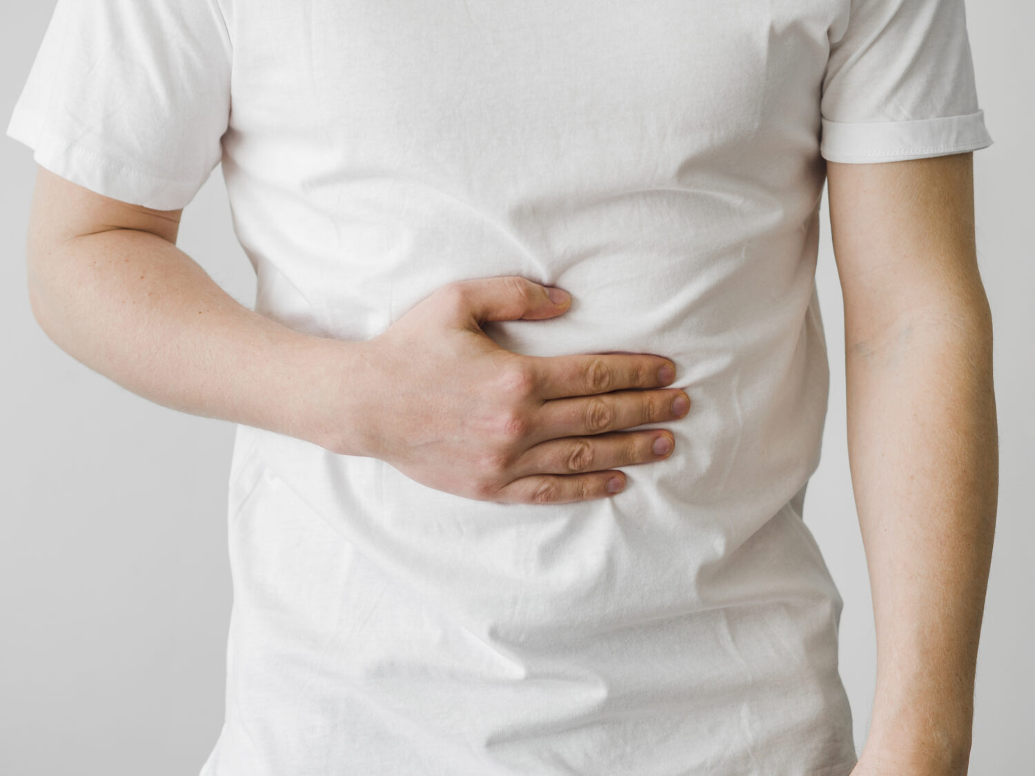 debloat, Man wearing a white t-shirt holds his stomach with his right hand.